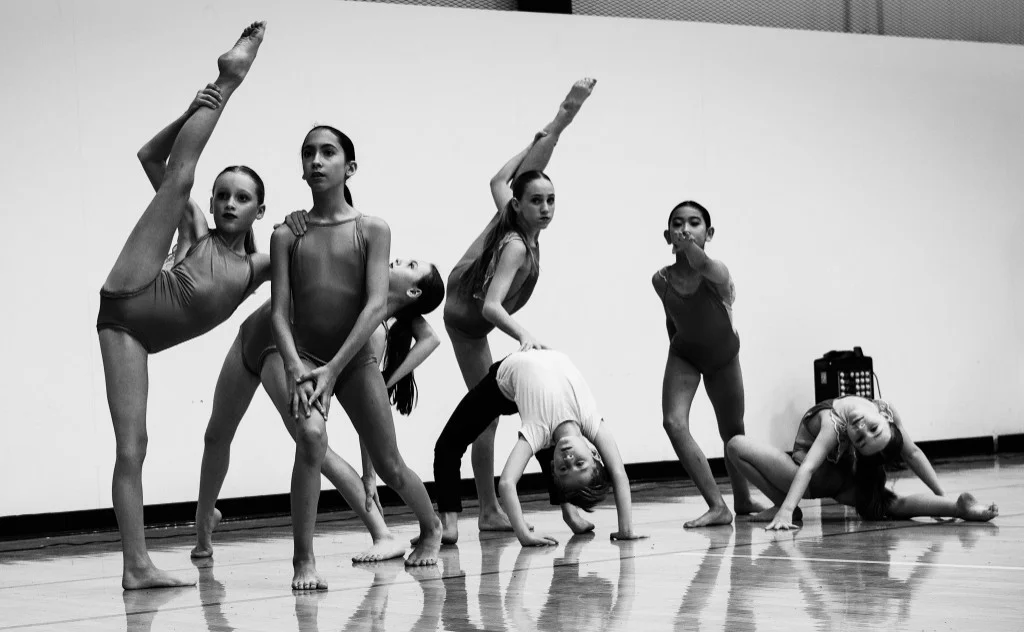 Fort Dance company members in a black-and-white portrait, posed together in extension, backbends, and contractions on a polished studio floor.