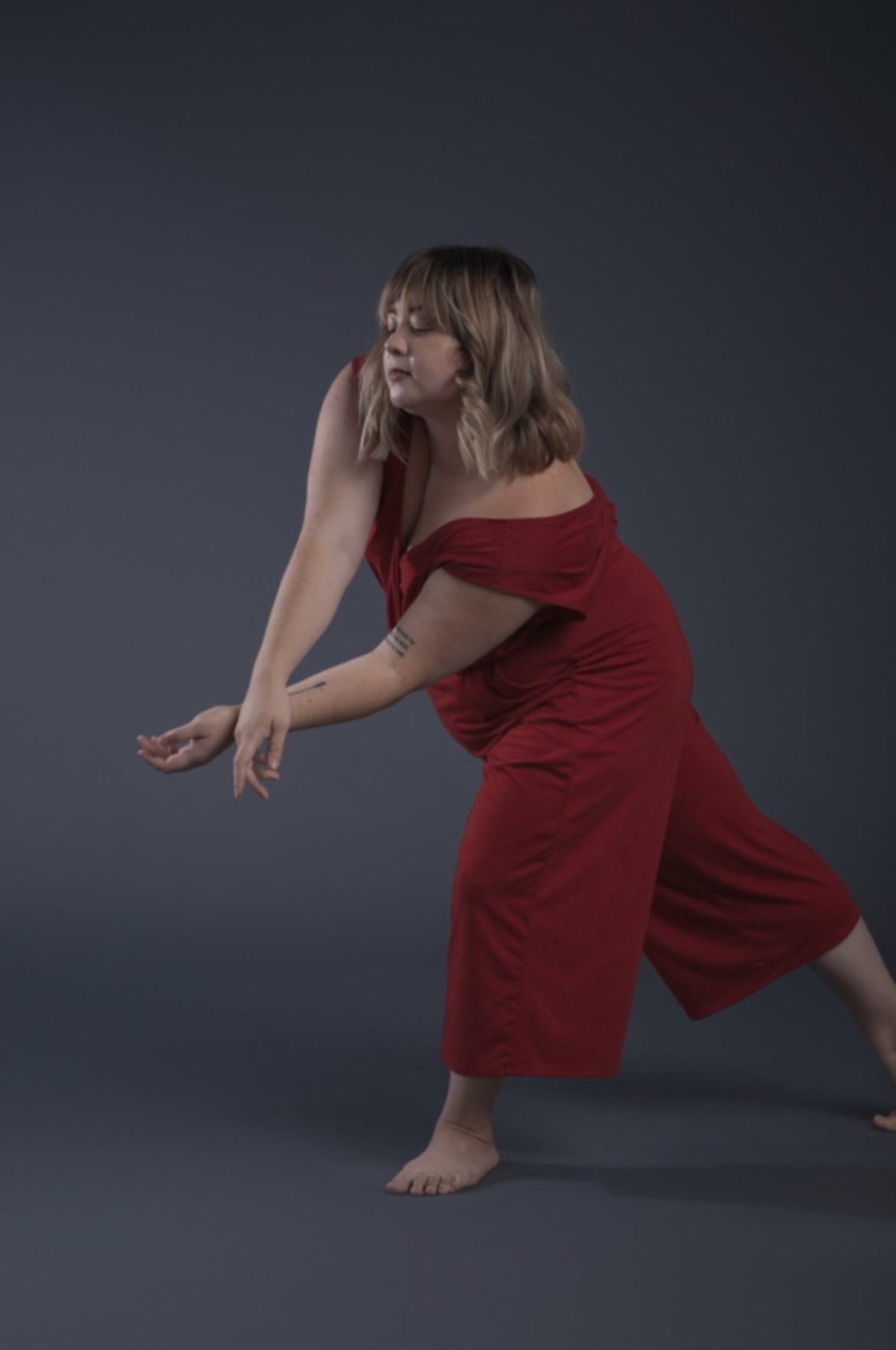Portrait of Brie Underwood-Duemig in a red dress, mid-movement against a dark gray backdrop
